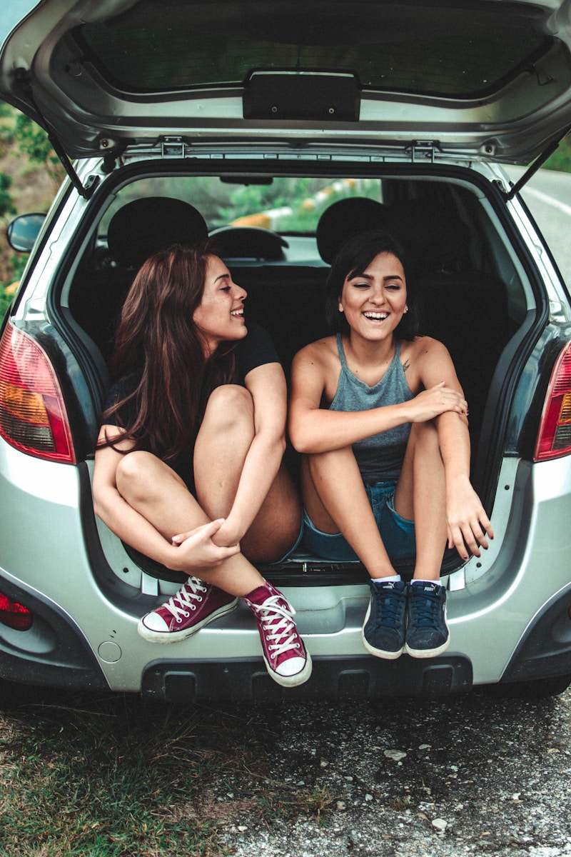 Two girls sitting in the trunk of a hatchback – Exploring the topic of car insurance policies and whose name can be on the policy.